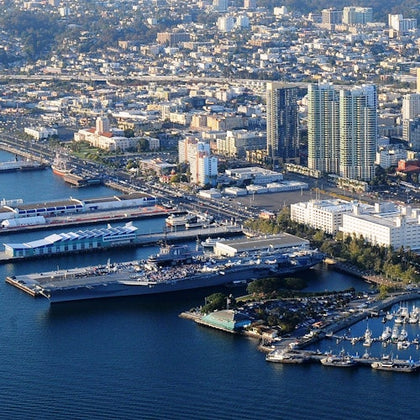 Aerial view of a coastal city with tall buildings, harbor, docked ships, and waterfront buildings.