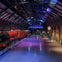 An indoor train station display with a red steam locomotive on tracks, surrounded by a well-lit arched roof and station decor.