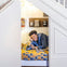 A person smiles while lying on a bed in a cozy space under stairs, decorated with a yellow patterned blanket and shelves.