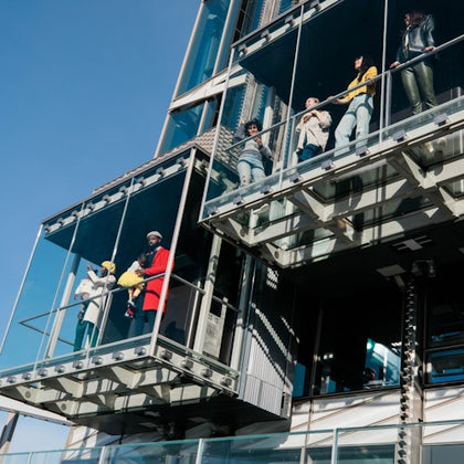 People standing on modern glass balconies attached to a building, with a clear blue sky in the background.