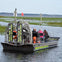 A group of people on an airboat with "Boggy Creek Airboat Adventures" signage, navigating through a marshy area.