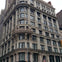 A historic multi-story building with ornate architectural details, large windows, and a flag displayed at its base.