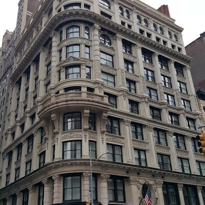 A historic multi-story building with ornate architectural details, large windows, and a flag displayed at its base.