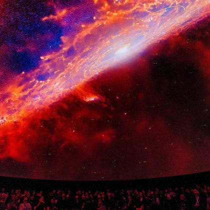 A crowd of people observing a vivid cosmic projection of a galaxy's center in a dark theater-like environment.