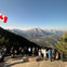People stand on a viewing platform overlooking a vast mountainous landscape with a Canadian flag flying.