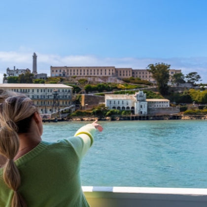 A person pointing towards a historic building complex across the water under a clear sky.