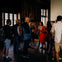 A group of people attentively listening to a presenter in a dimly lit room with wooden floors and large windows.