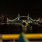 Tower Bridge illuminated at night with reflections on the Thames and buildings in the background.