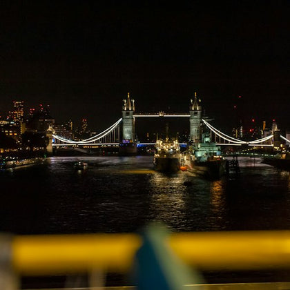 Tower Bridge illuminated at night with reflections on the Thames and buildings in the background.