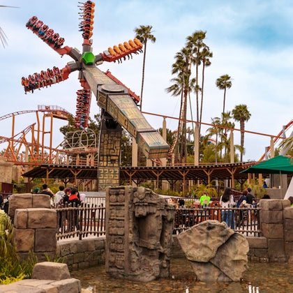Amusement park scene with a spinning ride, roller coaster tracks in the background, and decorative stone sculptures in the foreground.