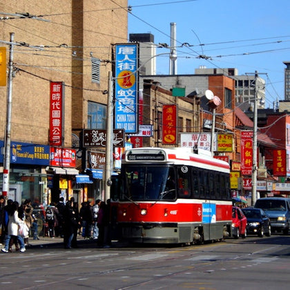 A red and white streetcar travels down a busy Chinatown street, surrounded by buildings with colorful signs and pedestrians.