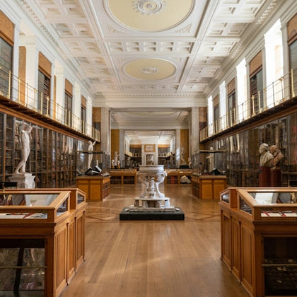 A brightly lit museum hall with glass display cases, sculptures, and a high ornate ceiling.
