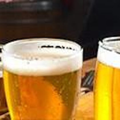 Two glasses of beer with foamy heads on a table, with a blurry background.