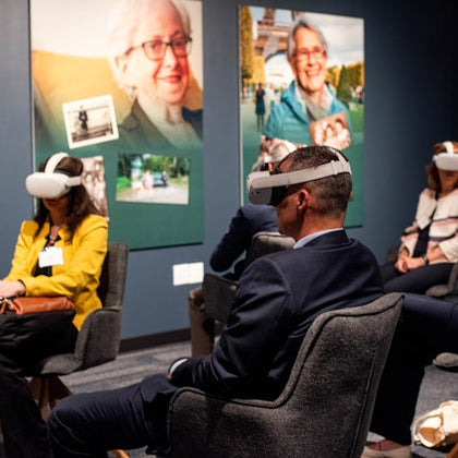People seated in a room wearing virtual reality headsets, with large portraits displayed on the wall behind them.