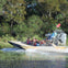 A group of people in life vests ride an airboat through a lush, swampy area with trees and grass.