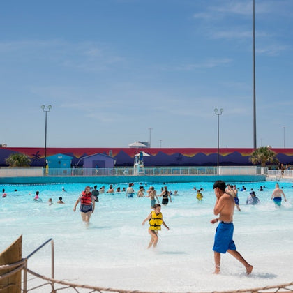 People enjoying a wave pool at a water park under a clear blue sky.