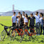 A group of friends pose in front of the bridge with their bikes