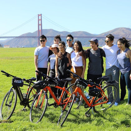 A group of friends pose in front of the bridge with their bikes