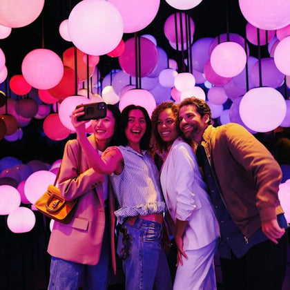 Four people taking a selfie in a room filled with glowing, colorful orbs hanging from the ceiling.