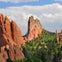 Tall red rock formations surrounded by green vegetation under a blue sky with clouds.
