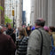 A group of people listening to a guide on a city street with tall buildings and a church visible in the background.