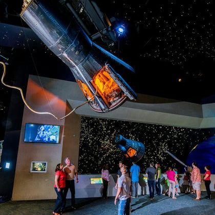 People viewing space capsules and starry exhibits in a space museum.