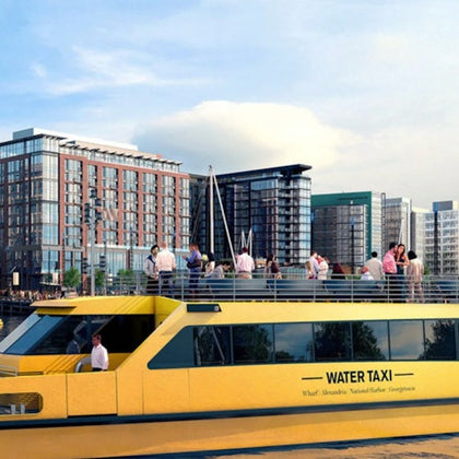 A yellow water taxi with passengers on the top deck in front of a waterfront urban area with modern buildings.