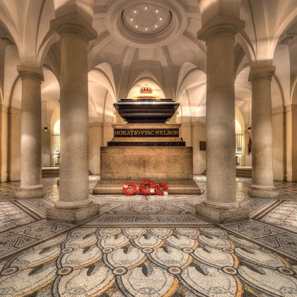 A grand crypt with stone columns, ornate flooring, and a central tomb with the inscription 'Horatio Viscount Nelson'.
