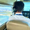 Pilot wearing headphones flying a plane with a view of the coastline and cityscape visible through the cockpit window.