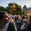 A group of people on an open-top bus tour observing and taking photos near a historic building at dusk.