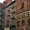 A city street with brick buildings featuring fire escapes and a traffic light suspended above the intersection.