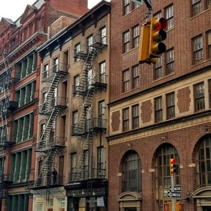 A city street with brick buildings featuring fire escapes and a traffic light suspended above the intersection.
