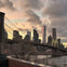 Brooklyn Bridge at dusk with New York City skyline in the background, featuring the One World Trade Center and cloudy sky.