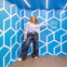 A person stands in a blue room with geometric wall patterns and a sign reading 'Museum of Illusions Manchester.'