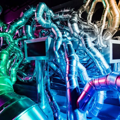 A labyrinth of shiny metallic pipes illuminated by colorful lights, with rectangular screens integrated into the structure.