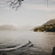 A person rides a jet ski on a calm lake surrounded by mountains and trees under a cloudy sky.