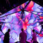 Three people stand in front of a geometric structure displaying vibrant, abstract visuals in purple and pink hues.