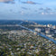 Aerial view of a coastal city with residential areas, high-rise buildings, and a waterway leading to the ocean under a partly cloudy sky.