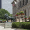 Two lion statues flank the entrance to a large building with flags, ornate planters, and lush greenery on a sunny day.