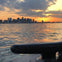A city skyline at sunset across a body of water with a metal dock cleat in the foreground.
