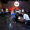 A child and an adult pose for a photo near a Batmobile at an exhibit, with other people and vehicles in the background.