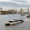 A river scene with an 'Uber Boat' catamaran on the Thames near Tower Bridge in London, with city buildings in the background.