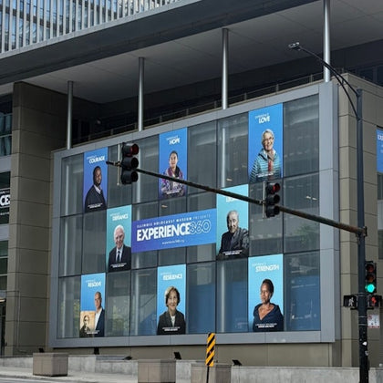 A building facade displaying posters for an exhibition titled "Experience 360," featuring portraits and inspirational words.