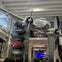 An airplane suspended indoors with a display of vintage cars mounted on a wall in a museum setting.