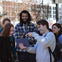 A group of people outdoors looking at a tablet, with some smiling and one person pointing at the screen.
