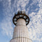 A modern tower with a glass observation deck against a sky with scattered clouds.