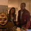 Two people smile while looking at an intricate antique clock in a museum display case.