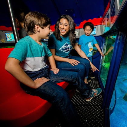 A woman and two children look at aquatic life through a glass panel inside a colorful underwater-themed exhibit.