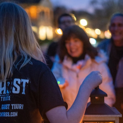 Tour guide holding a lantern as guests surround her to listen to ghost stories
