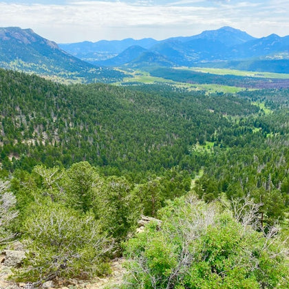 A scenic view of a lush green valley surrounded by forested mountains under a partly cloudy sky.